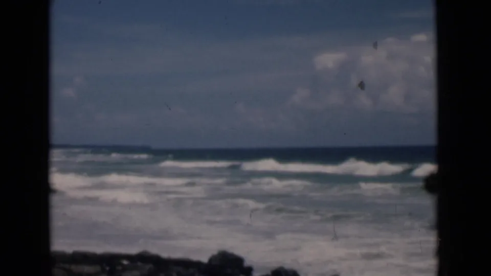 1946 Colombo, Ceylon beach view with surf rolling toward pale sand, framed by a dark doorway or window edge.