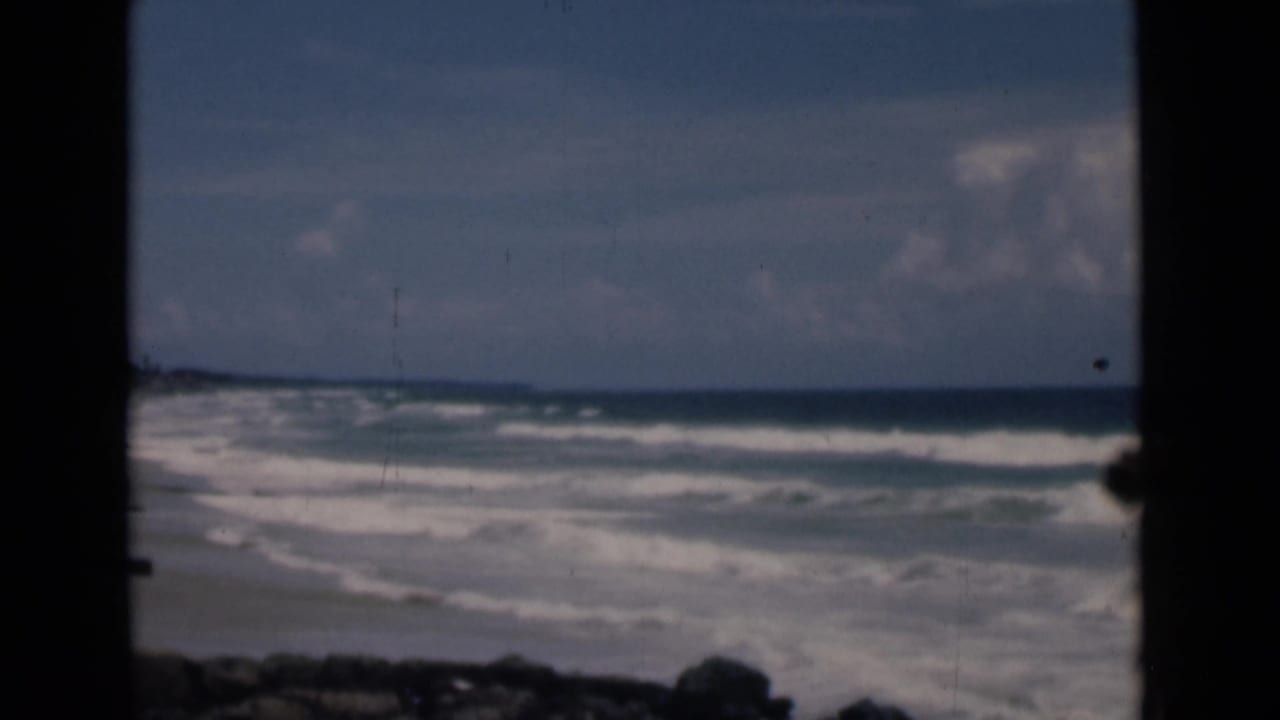 White surf and distant shoreline framed by a dark central vertical edge.
