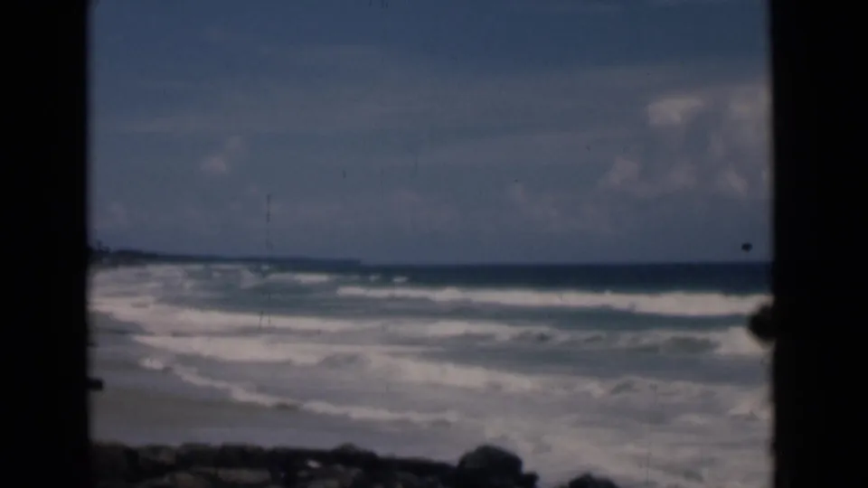 Mid-1940s 8mm view of Colombo surf under a blue sky, with a dark window or doorway frame splitting the scene.