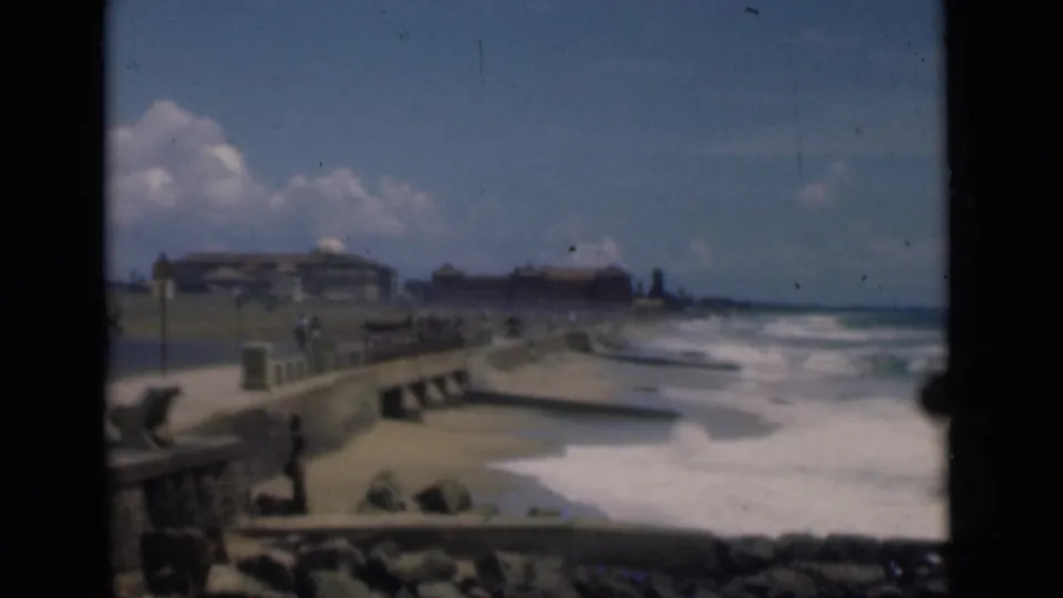Colombo, Ceylon beach scene from 1946 with a stone seawall, surf, rocks, low buildings, and distant people along the waterfront.