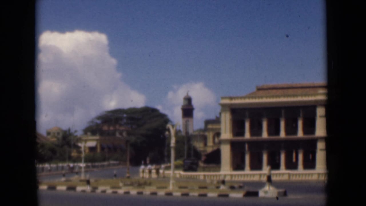 Colonnaded building beside a broad street with a distant clock tower and pedestrians.