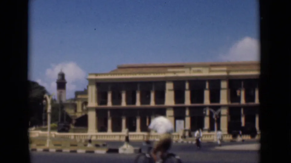 1946 Colombo street view with a colonnaded building, distant pedestrians, clock tower, and a bicyclist passing near the foreground.