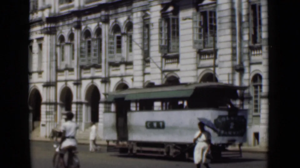 1946 Colombo view of a streetcar moving past a grand arched colonial-style building with pedestrians and a cyclist nearby.