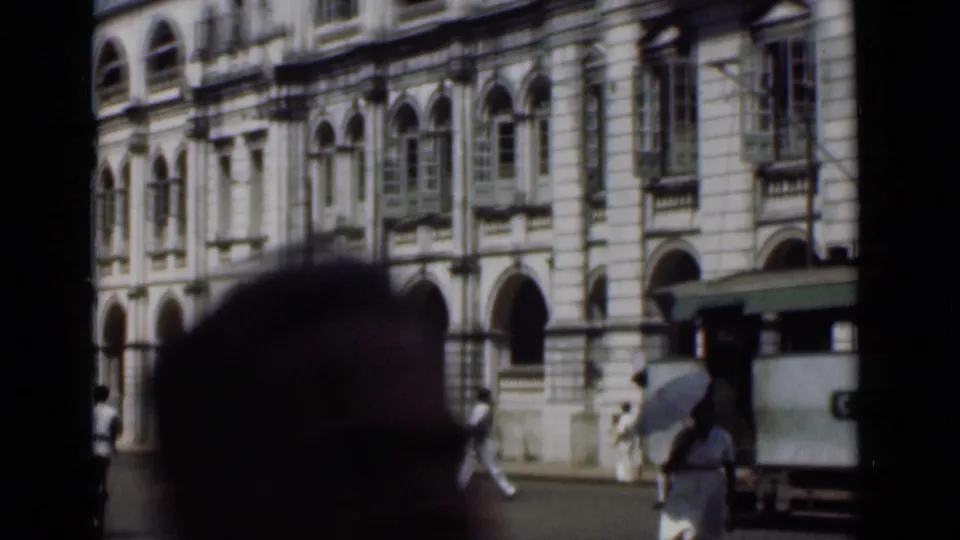 1946 Colombo streetcar scene with pedestrians beside an arched colonial-style facade and a blurred foreground head at the bottom of frame.