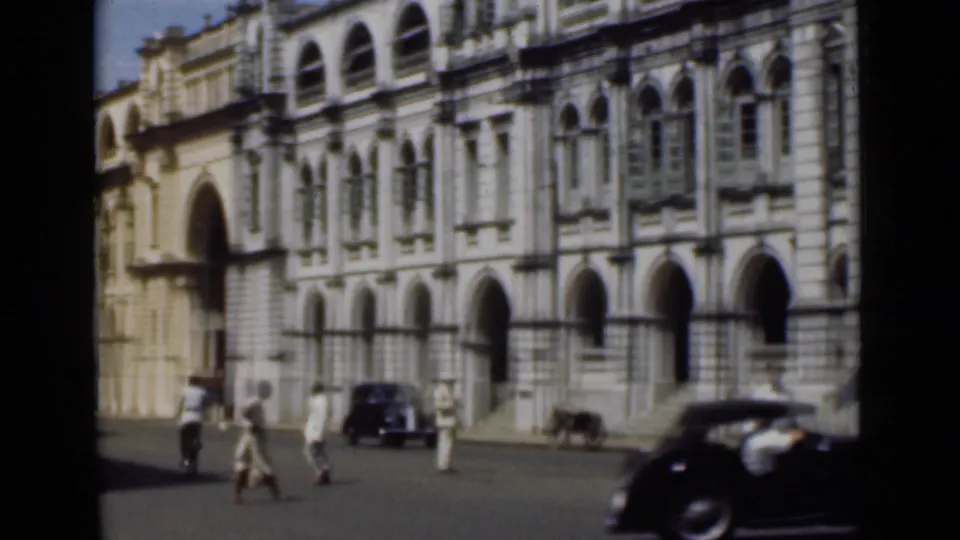1946 Colombo street scene with pedestrians crossing before an arched colonial-style facade and vintage cars.