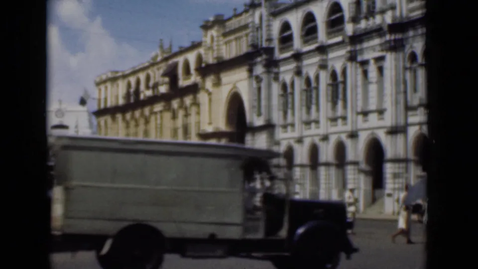1946 Colombo street footage with a delivery truck moving in front of pedestrians and a colonial-style building facade.