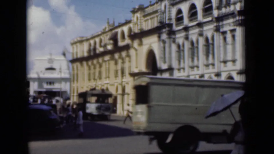 1946 Colombo street view with a delivery truck passing colonial-era arched buildings and pedestrians near a white building in the distance.