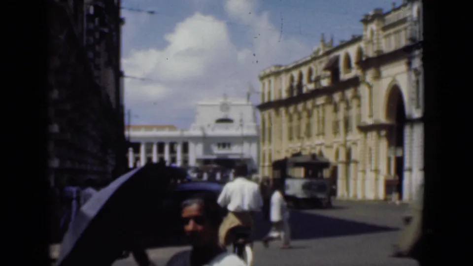 Street-level 1946 Colombo view with pedestrians, a shaded umbrella, a bus or truck, and colonial-era arched architecture.