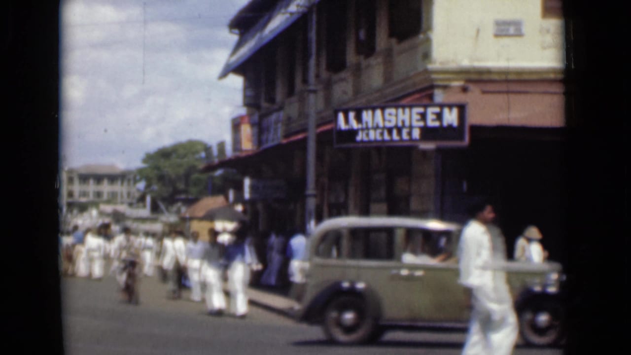 Busy Colombo street corner with pedestrians, a green vintage car, and an A. Hasheem Jeweller sign.