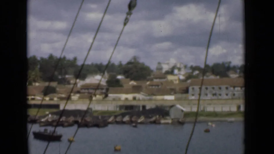1946 Colombo harbor view from a ship, with rigging crossing the frame and low waterfront buildings beyond the water.