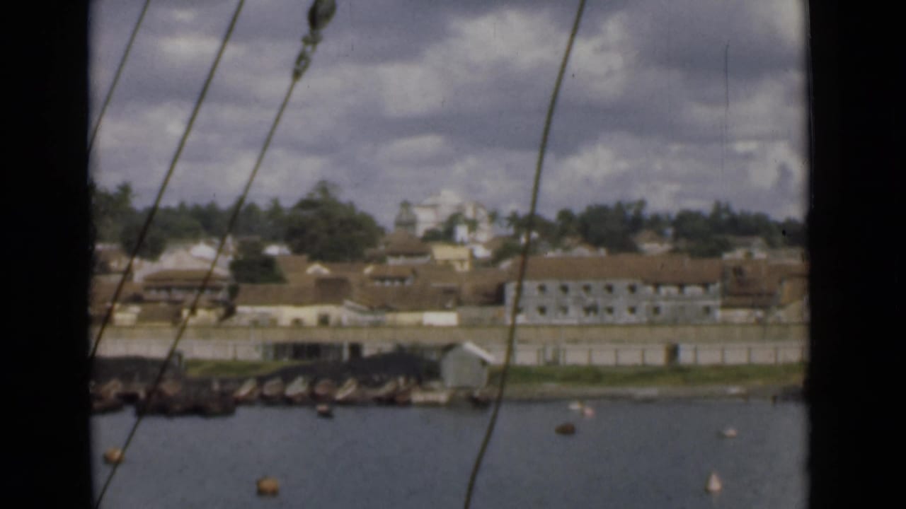 Distant shoreline with tiled-roof buildings, water, buoys, and rigging lines.