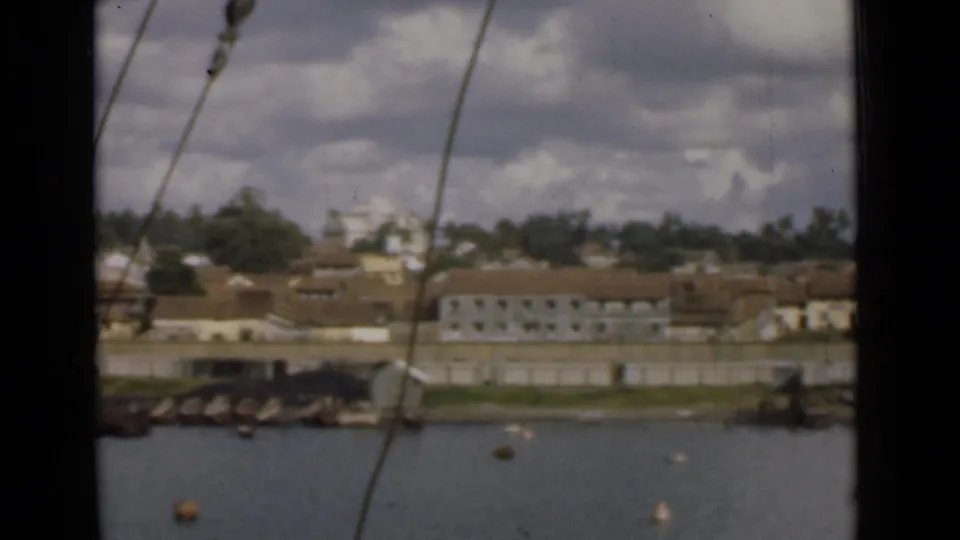 Colombo waterfront seen from the water in 1946, with a quay, pale buildings, tiled roofs, and rigging in front.