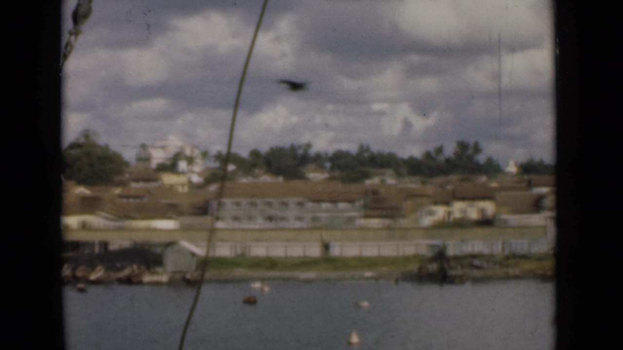 1946 shipboard view across Colombo harbor, showing rigging, scattered buoys, small craft, and waterfront buildings.