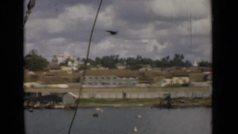 1946 shipboard view across Colombo harbor, showing rigging, scattered buoys, small craft, and waterfront buildings.