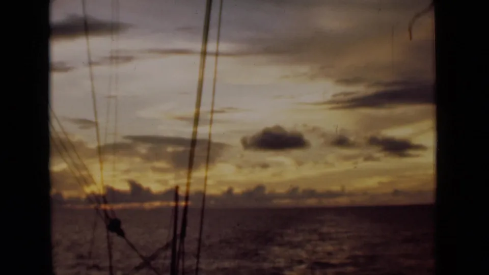 8mm home-movie still of a Colombo-area sea sunset, viewed past dark rigging from a sailing vessel.