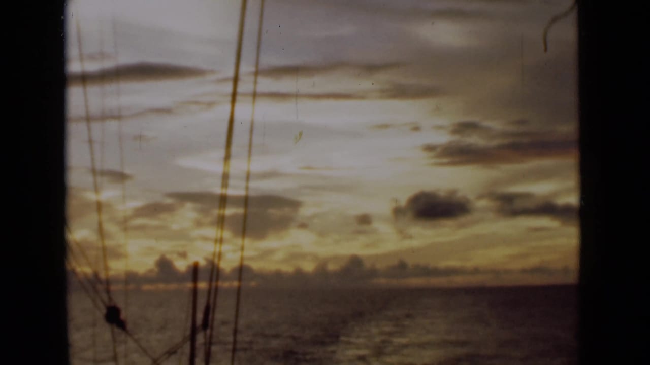 Warm sunset sky above the sea with sailboat rigging crossing the frame.