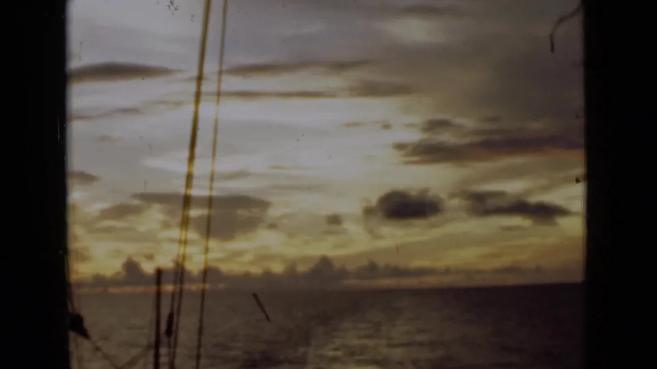 Vintage 8mm view near Colombo showing a dim ocean horizon, sunset clouds, and sailboat rigging silhouetted against the sky.