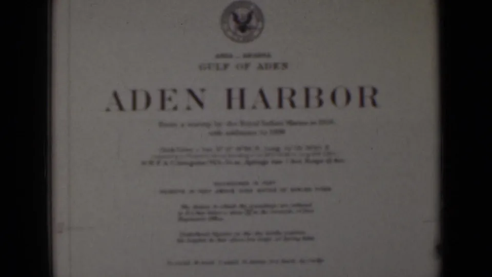 Soft 8mm frame of an Aden Harbor printed title card, showing a large title, emblem, and smaller unreadable text.