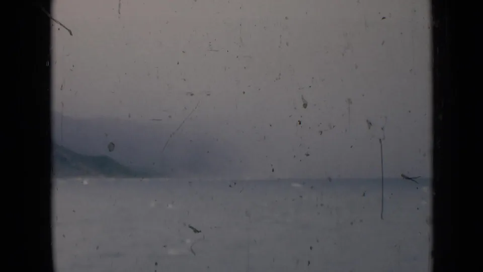1946 India 8mm frame with a pale cloudy sky, calm sea, and low hills near the horizon, marked by film wear.