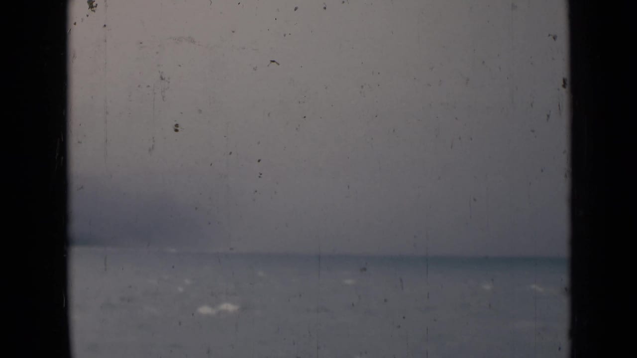 1946 India 8mm frame showing a misty body of water and faint horizon through dark window or railing bars.