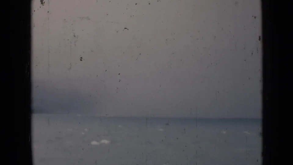 1946 India 8mm frame showing a misty body of water and faint horizon through dark window or railing bars.