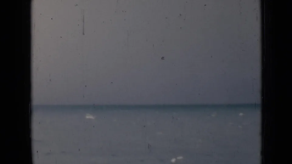 Grainy 8mm frame from India showing calm water under a hazy sky, partly blocked by dark vertical edges.