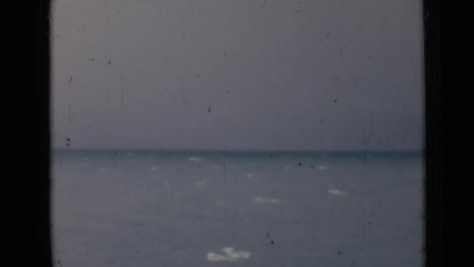 1946 India home-movie frame with calm water, faint wave highlights, and a hazy horizon behind dark framing.