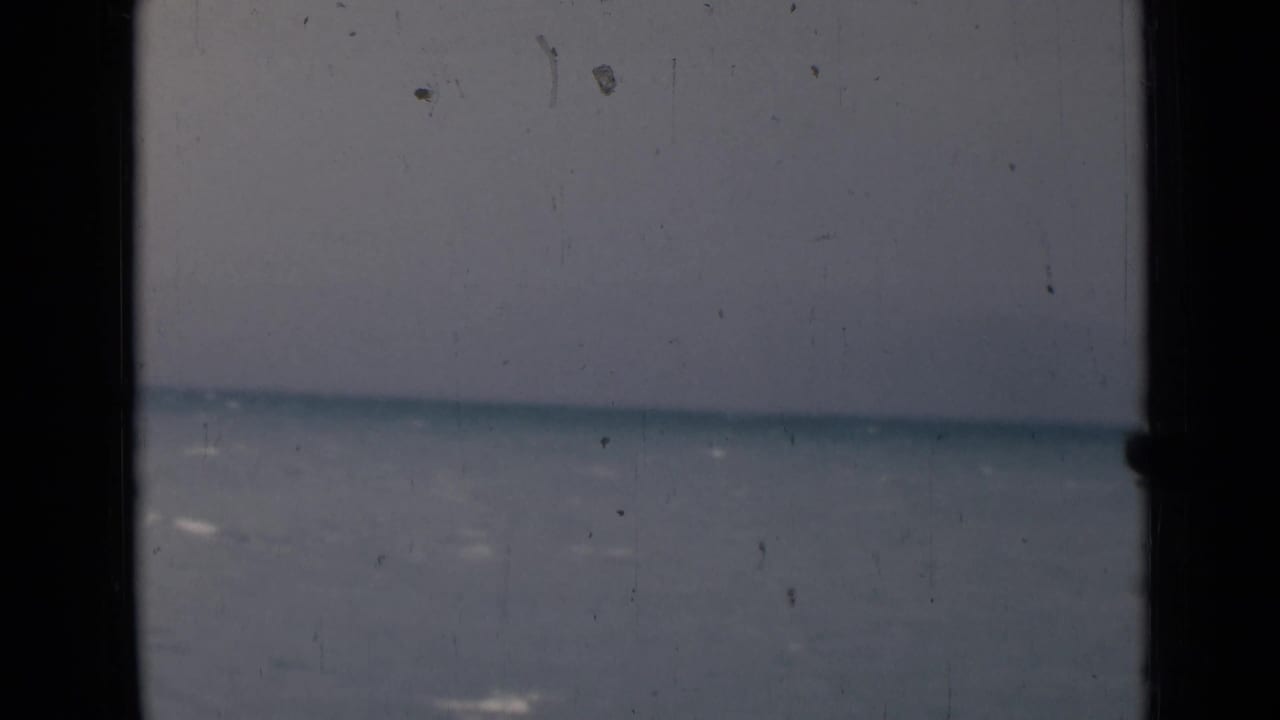 Calm blue-gray sea and horizon seen through dark window-frame bars.