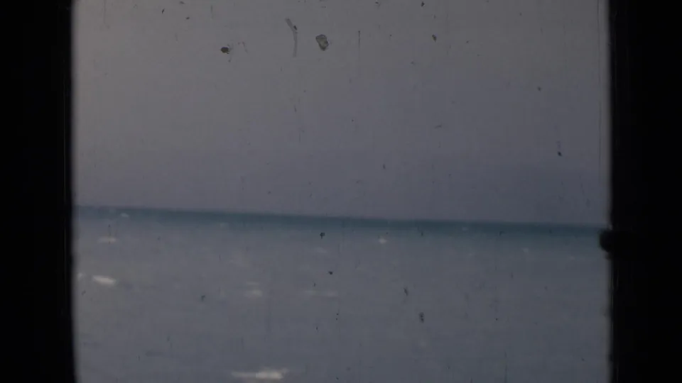 1946 India 8mm frame of calm sea and cloudy sky viewed through dark vertical window or rail supports, with no clear ship visible.