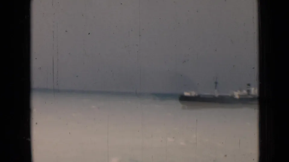 1946 India 8mm frame showing a distant large ship on the horizon, partly framed by dark vertical supports and aged film marks.