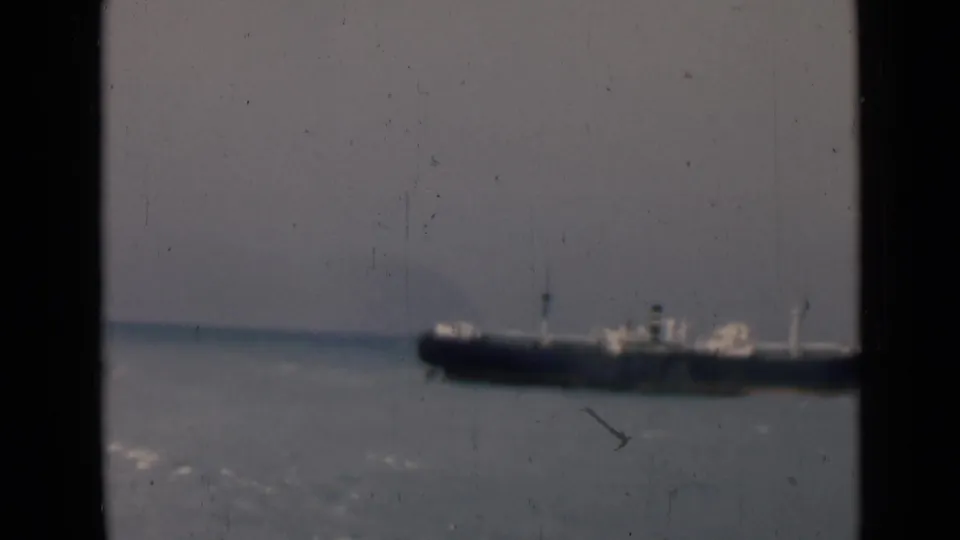 1946 India 8mm frame with a large distant ship on blue-gray water, viewed through dark foreground framing and visible film wear.
