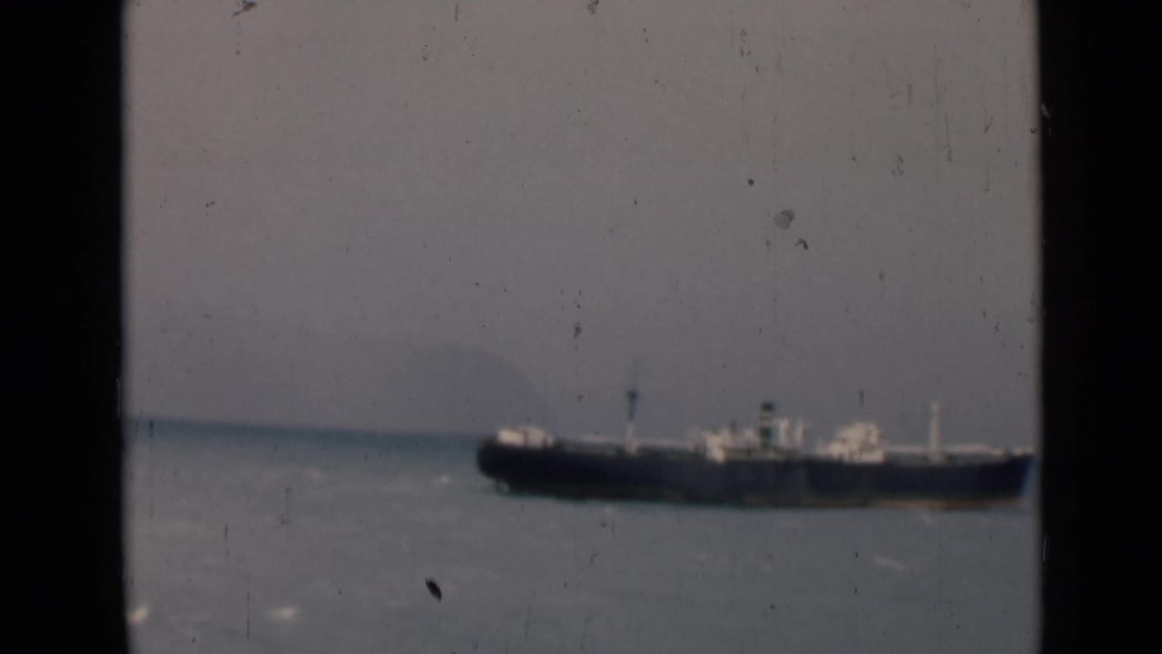 Large cargo ship on choppy water seen through dark vertical framing.
