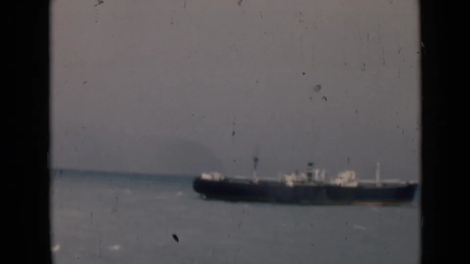 1946 India 8mm frame showing a large cargo ship offshore, partly enclosed by dark window or railing edges.