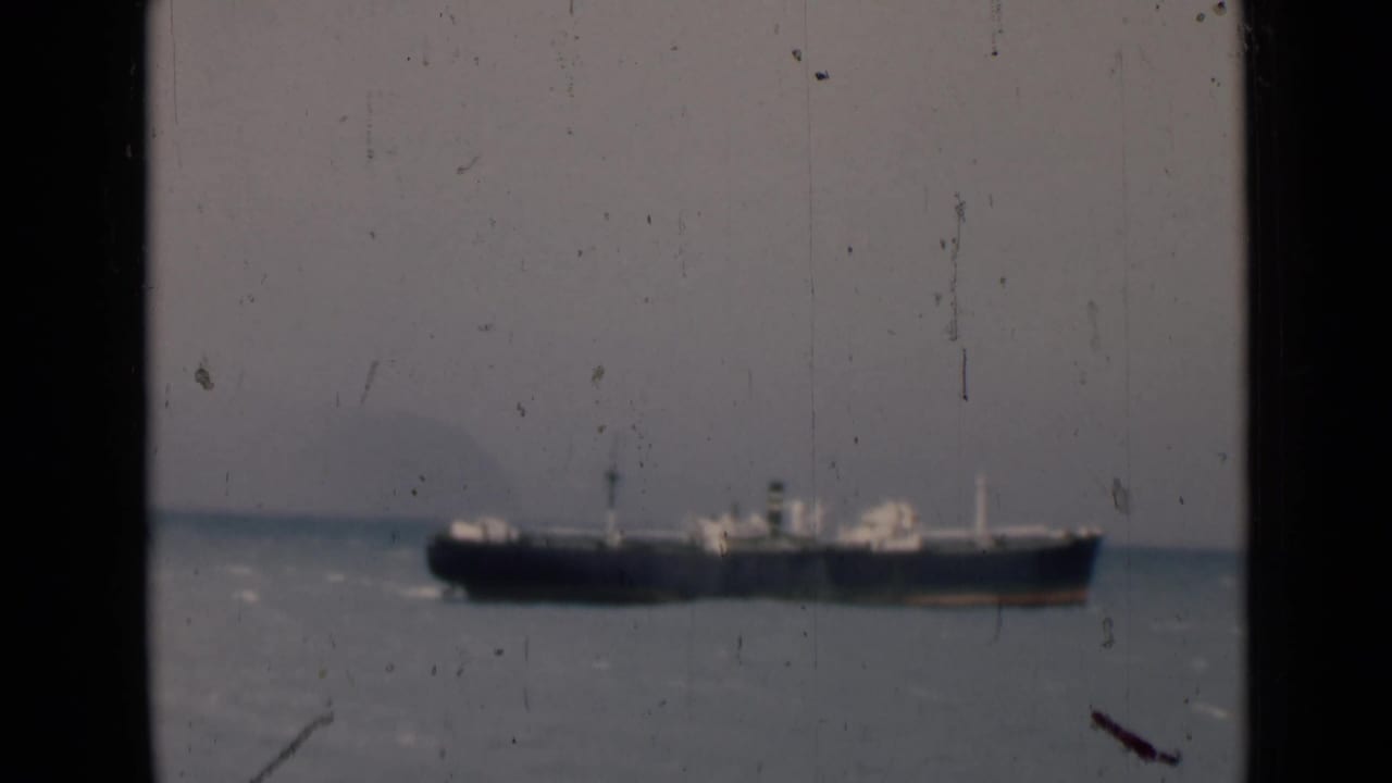 Cargo ship moving across open water with horizon and film wear visible.