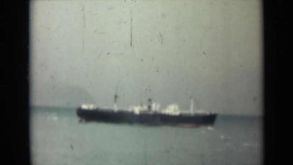 1946 India 8mm frame showing a dark-hulled cargo ship far offshore against calm water and a hazy sky.