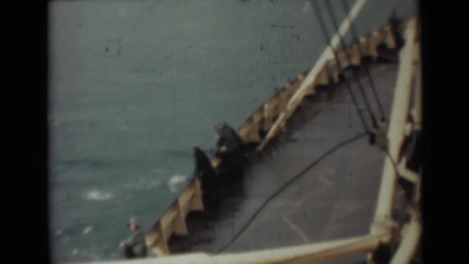 1946 India shipboard frame looking along the deck toward the bow, with railings, rigging lines, open sea, and a small figure near the edge.