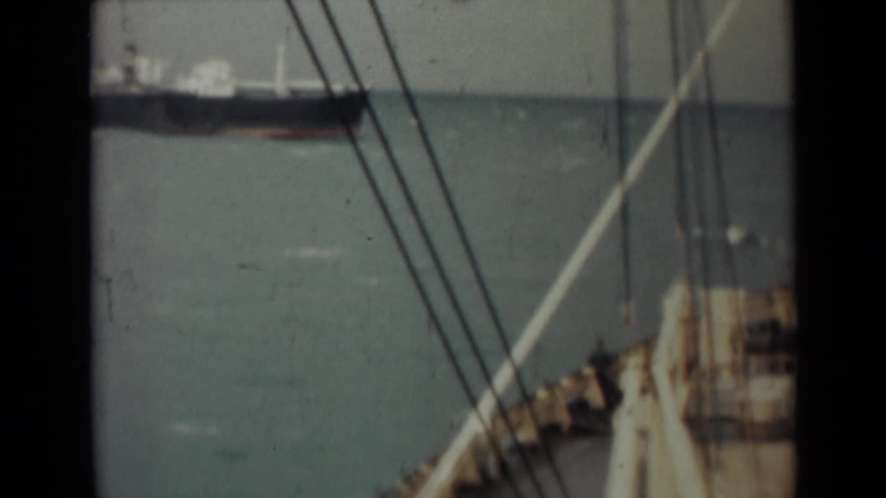 Rigging lines cross the view toward a distant dark ship on the water.