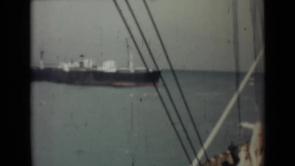 1946 India 8mm frame showing a distant freighter near the horizon, partly framed by rigging from another vessel.