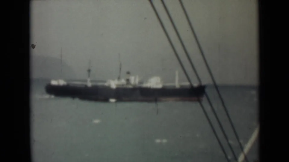 1946 India home-movie frame with a large cargo ship in the distance, seen through rigging from the filming vessel.