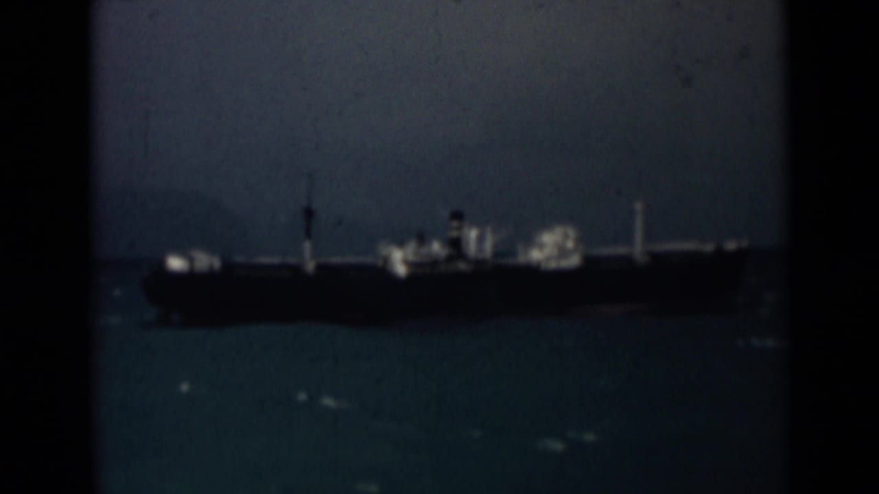 1946 8mm frame from India showing a distant cargo ship at sea with dark hull, white structures, and visible film borders.