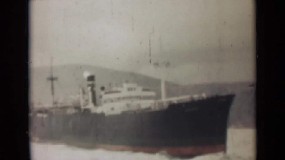 1946 India 8mm frame showing a large dark-hulled vessel on calm water, with a pale superstructure and distant hills in haze.