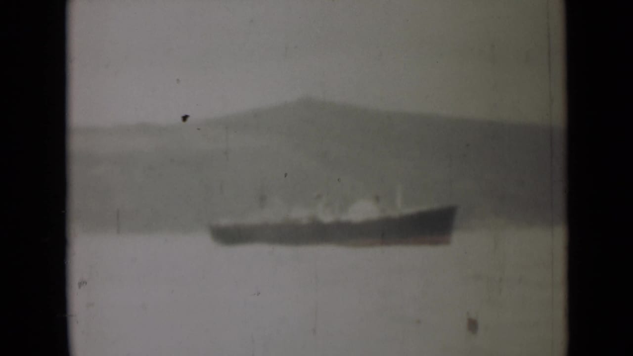 Distant vessel on still water below a hazy mountain ridge.