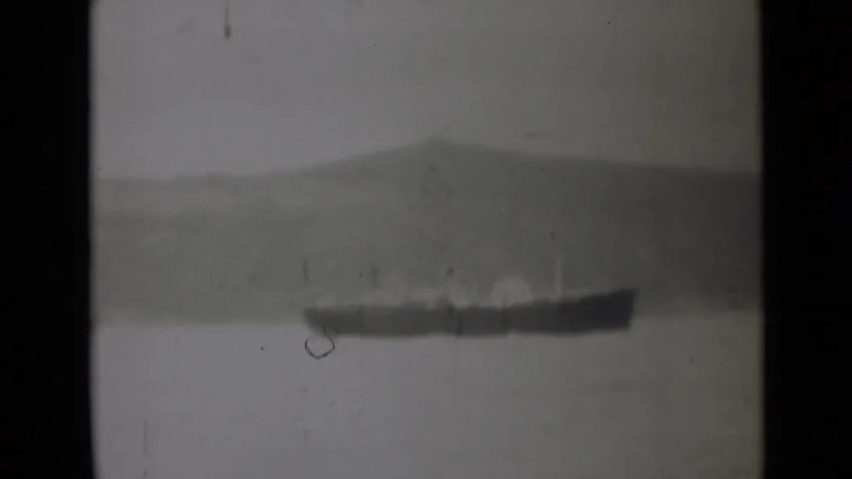 1946 India 8mm frame showing a small distant vessel on quiet water, framed by muted hills and visible film wear.