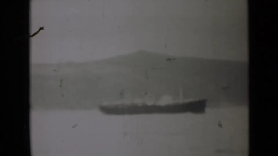 1946 India 8mm frame with a distant vessel moving or resting on calm water, backed by hazy hills and worn film texture.