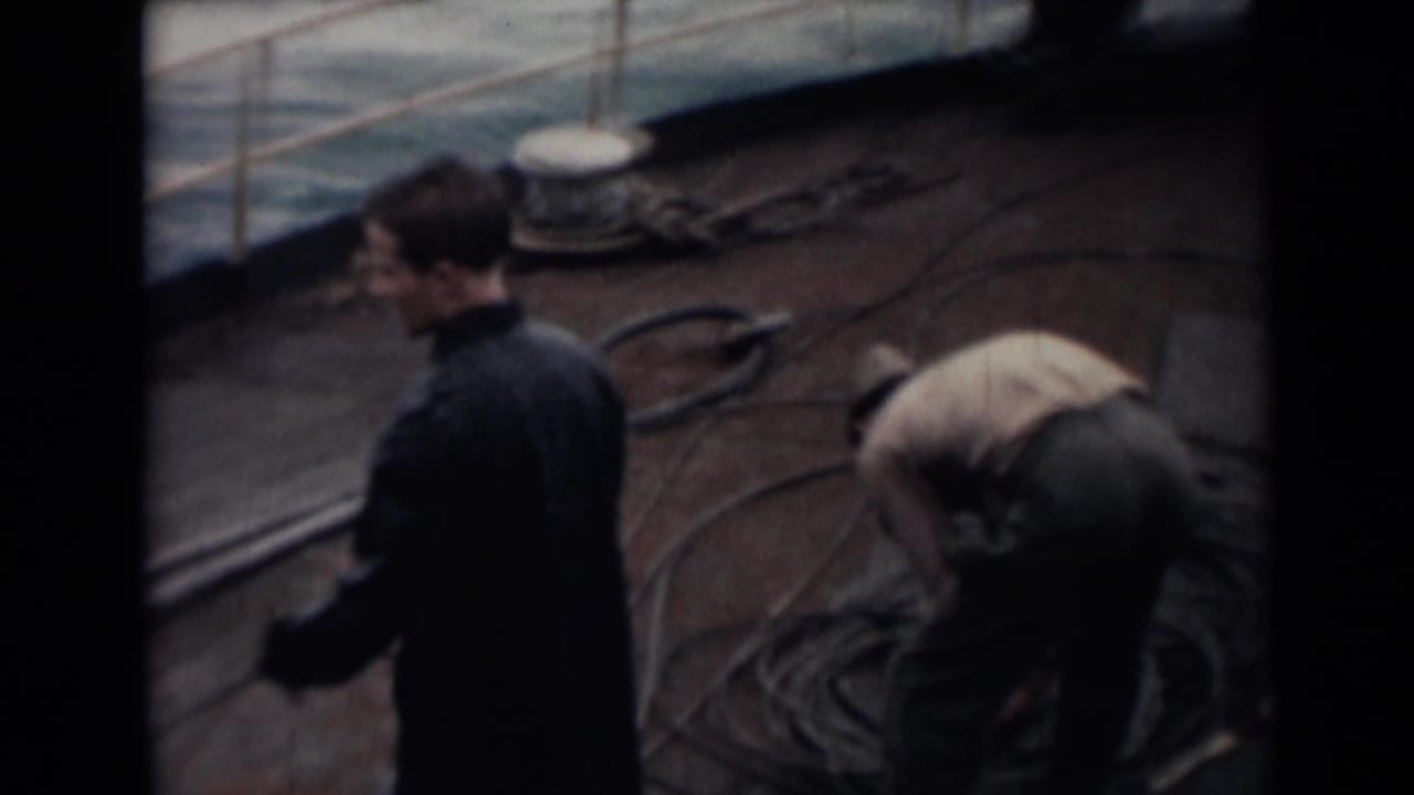 Two men on a ship deck near coiled rope, with ocean visible beyond the railing.