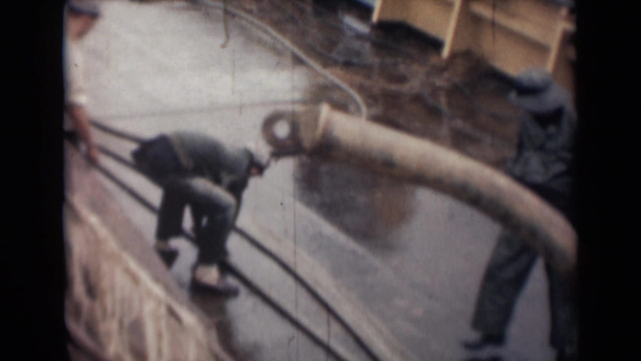 A man bends over on a wet ship deck near railings and a large hose.