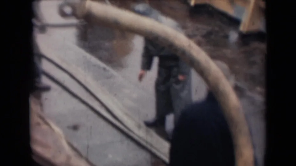 Crew members are partly visible around a large curved hose and deck railings in a soft 1940s shipboard frame.