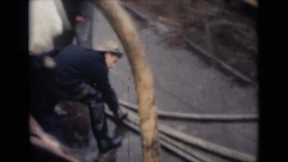A crew member in dark clothing leans near hoses and railings on a wet ship deck in 1946 India archival footage.