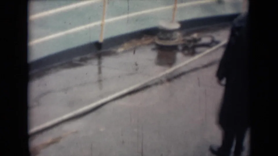 1946 India 8mm frame showing a rain-slick boat deck with white railing, bollard, rope, and a partially visible man in a dark coat.