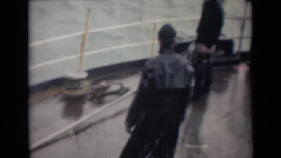 1946 India shipboard frame with men in dark rainwear on a reflective deck near coiled rope, deck hardware, and pale water beyond the rail.